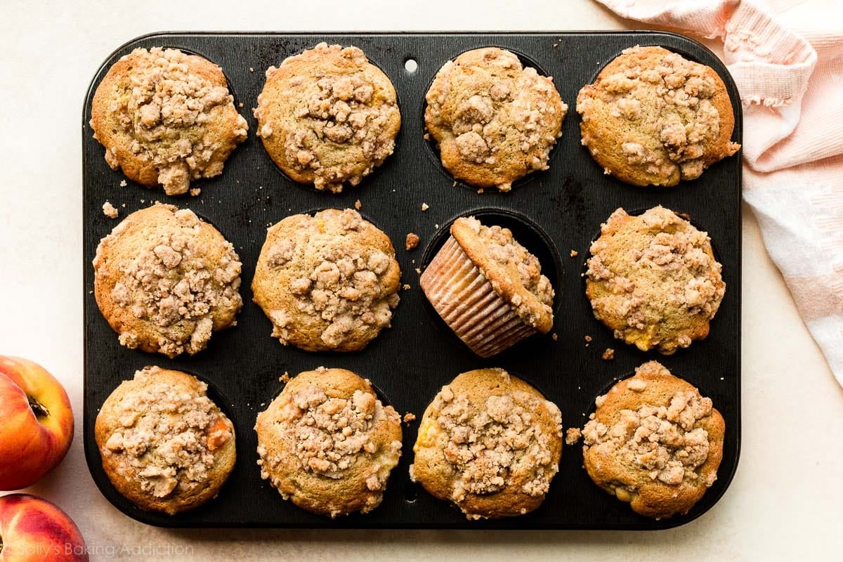 baked peach streusel muffins in black muffin pan.