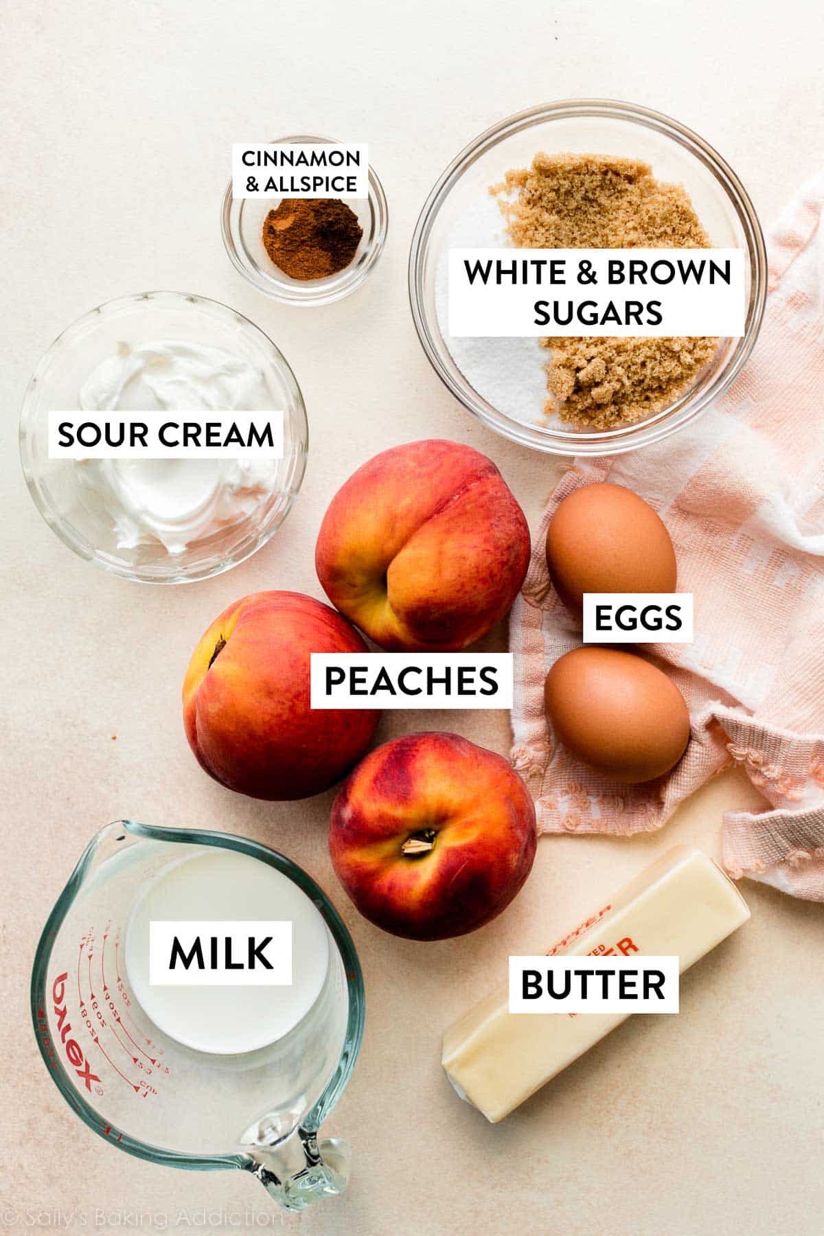 peaches, eggs, brown and white sugars, butter, milk, and other ingredients on peach backdrop.
