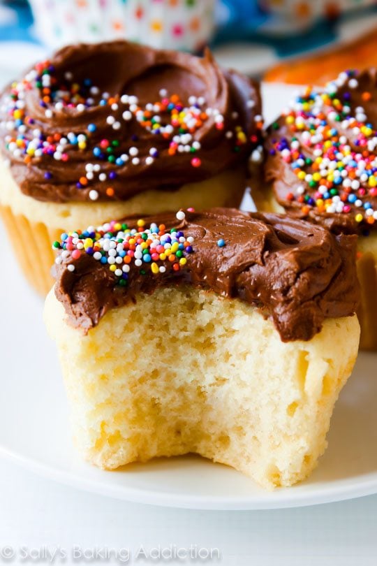 yellow cupcakes topped with milk chocolate frosting and sprinkles with a bite taken out of one cupcake
