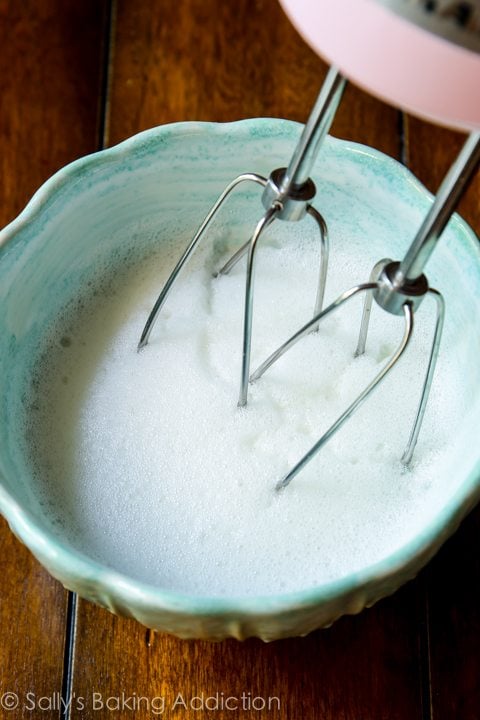 foamy egg whites in a blue bowl with a hand mixer