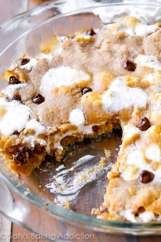 s'mores chocolate chip cookie cake in a glass baking dish with a slice removed