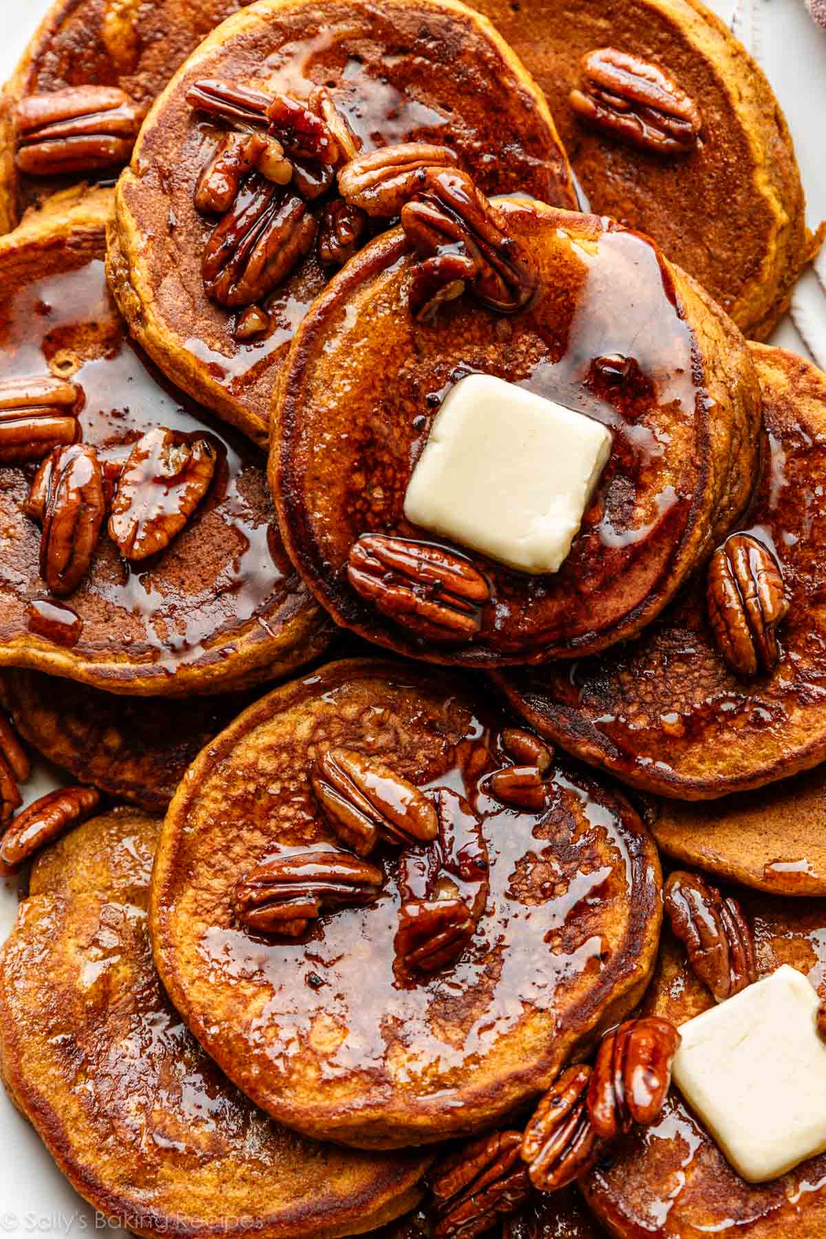 close-up of pumpkin pancakes with slices of butter and maple pecan syrup on top.