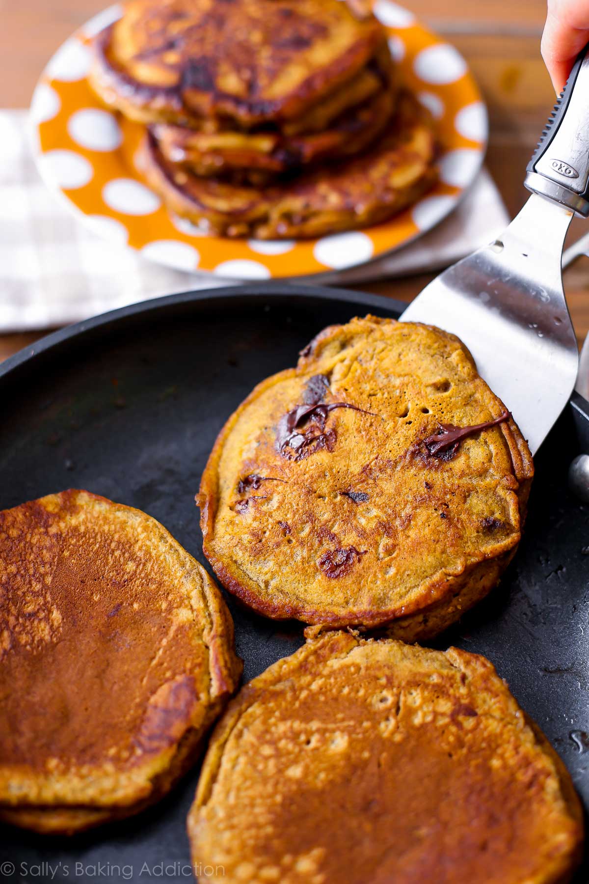 pumpkin chocolate chip pancakes in a skillet with a spatula
