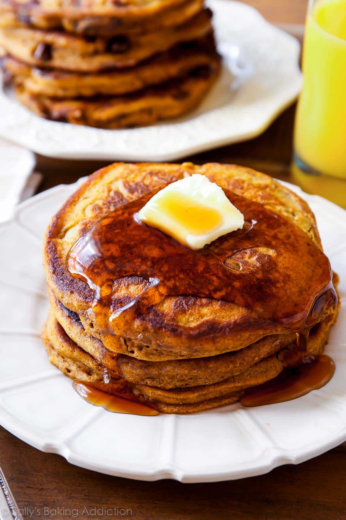 stack of pumpkin chocolate chip pancakes with maple syrup and butter on a white plate