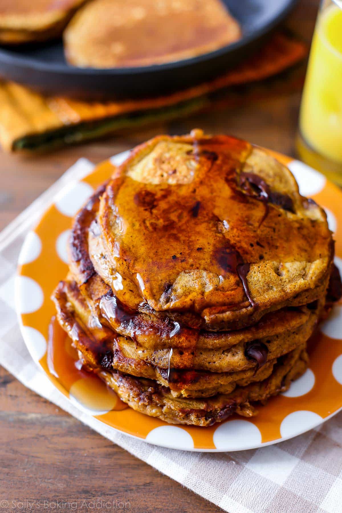 stack of pumpkin chocolate chip pancakes with maple syrup on an orange polka dot plate