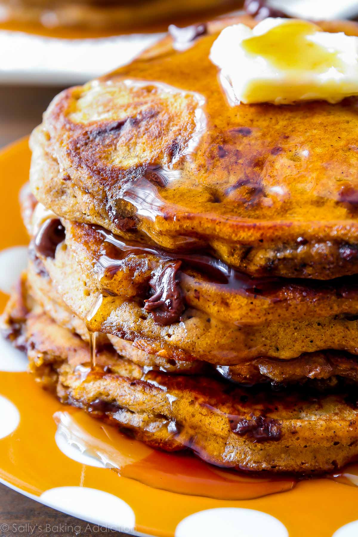 stack of pumpkin chocolate chip pancakes with maple syrup and butter on an orange polka dot plate