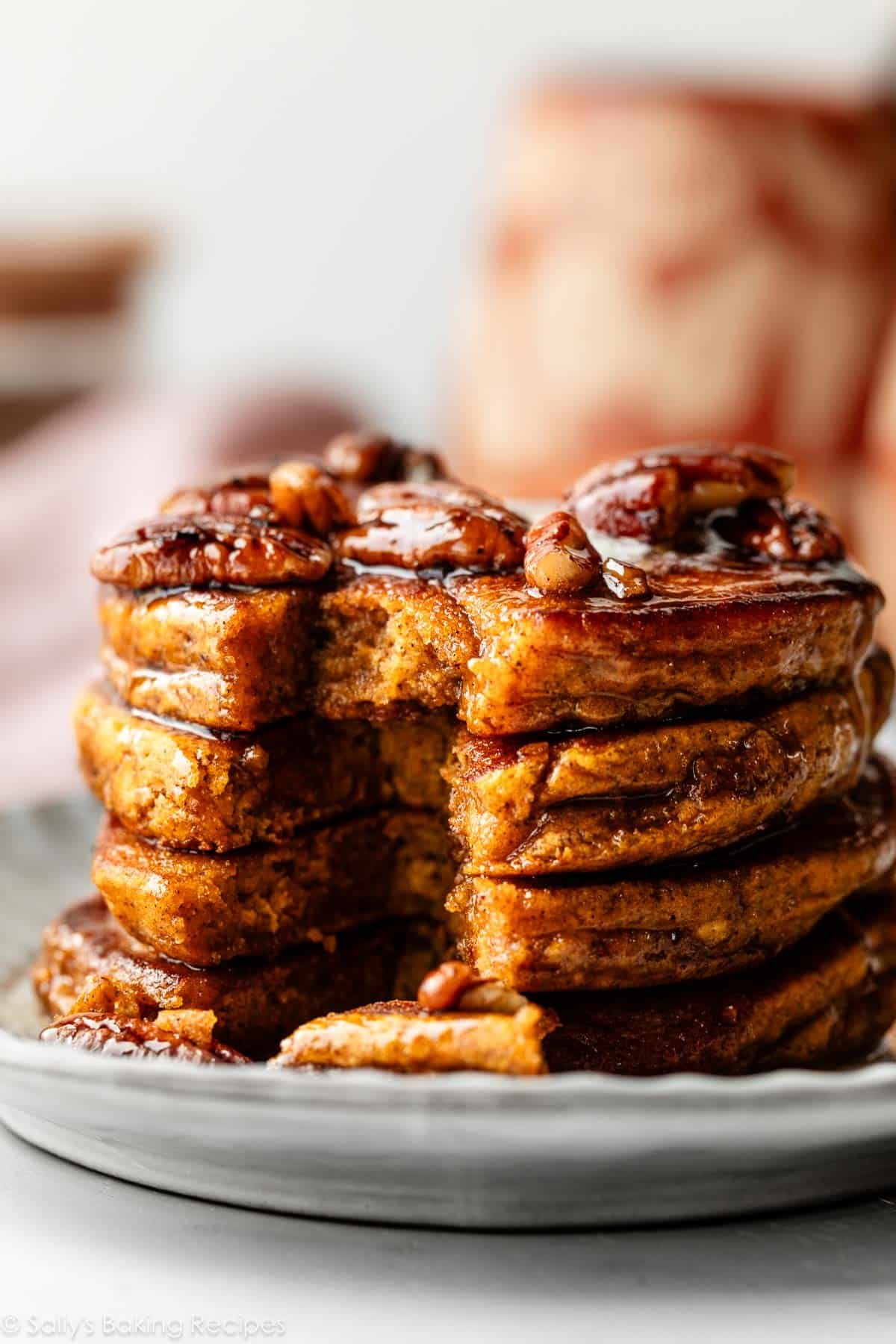 stack of pumpkin pancakes with pecans and maple syrup on top.
