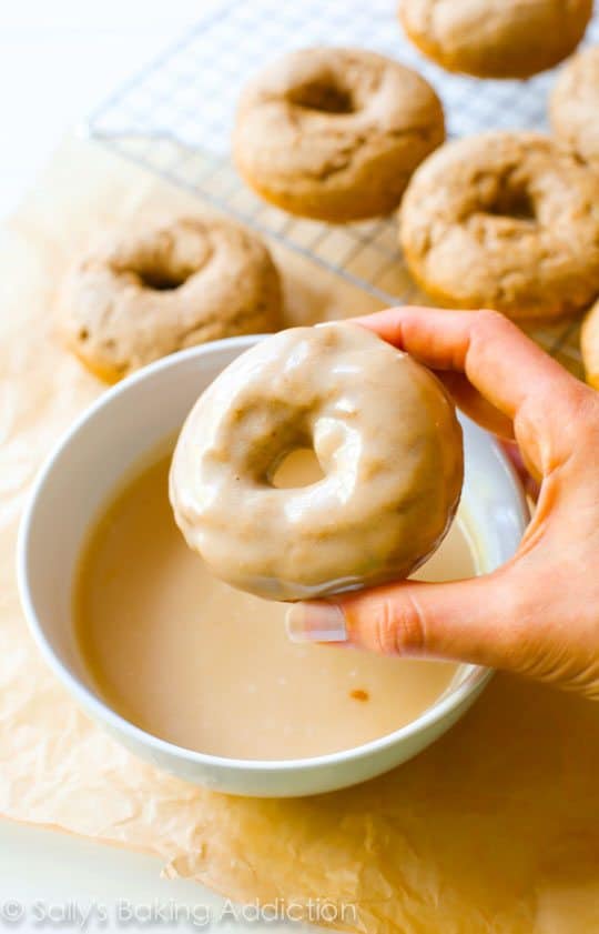 hand dipping a donut into a bowl of maple glaze