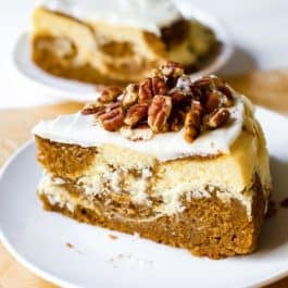 slice of pumpkin cake cheesecake with cream cheese frosting on a white plate