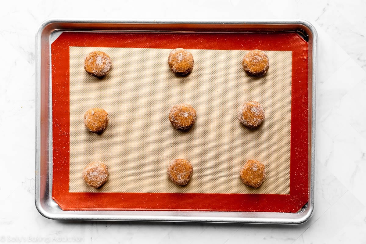 pumpkin cookie dough shaped into flat balls on lined cookie sheet.