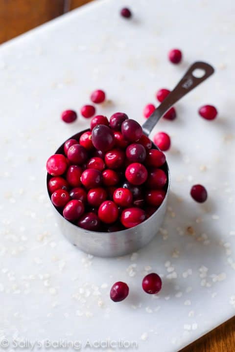 cranberries in a measuring cup on a white cutting board