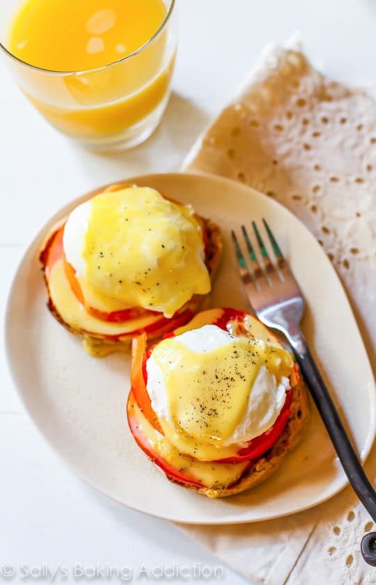 overhead image of eggs benedict on a white plate with a fork and glass of orange juice