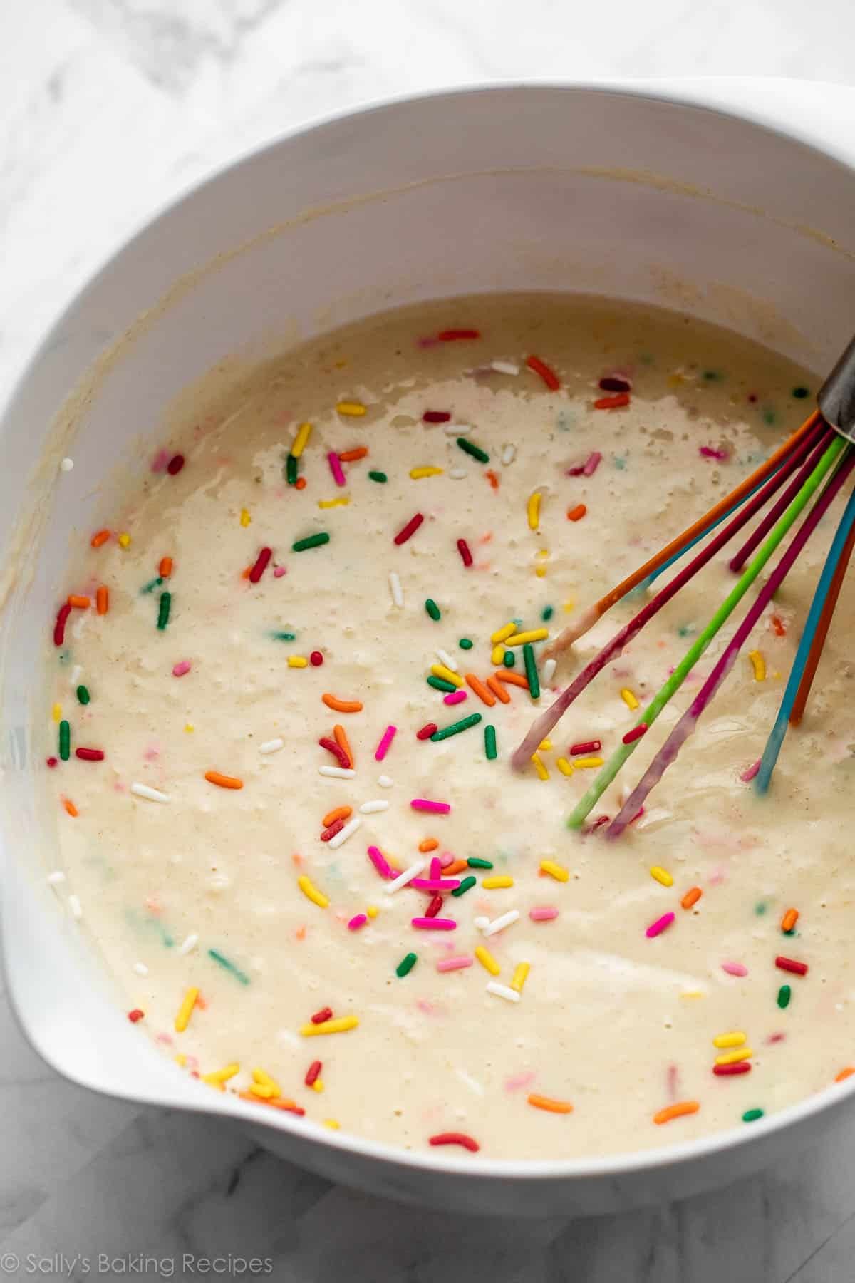 sprinkle buttermilk pancake batter in white bowl with rainbow whisk.