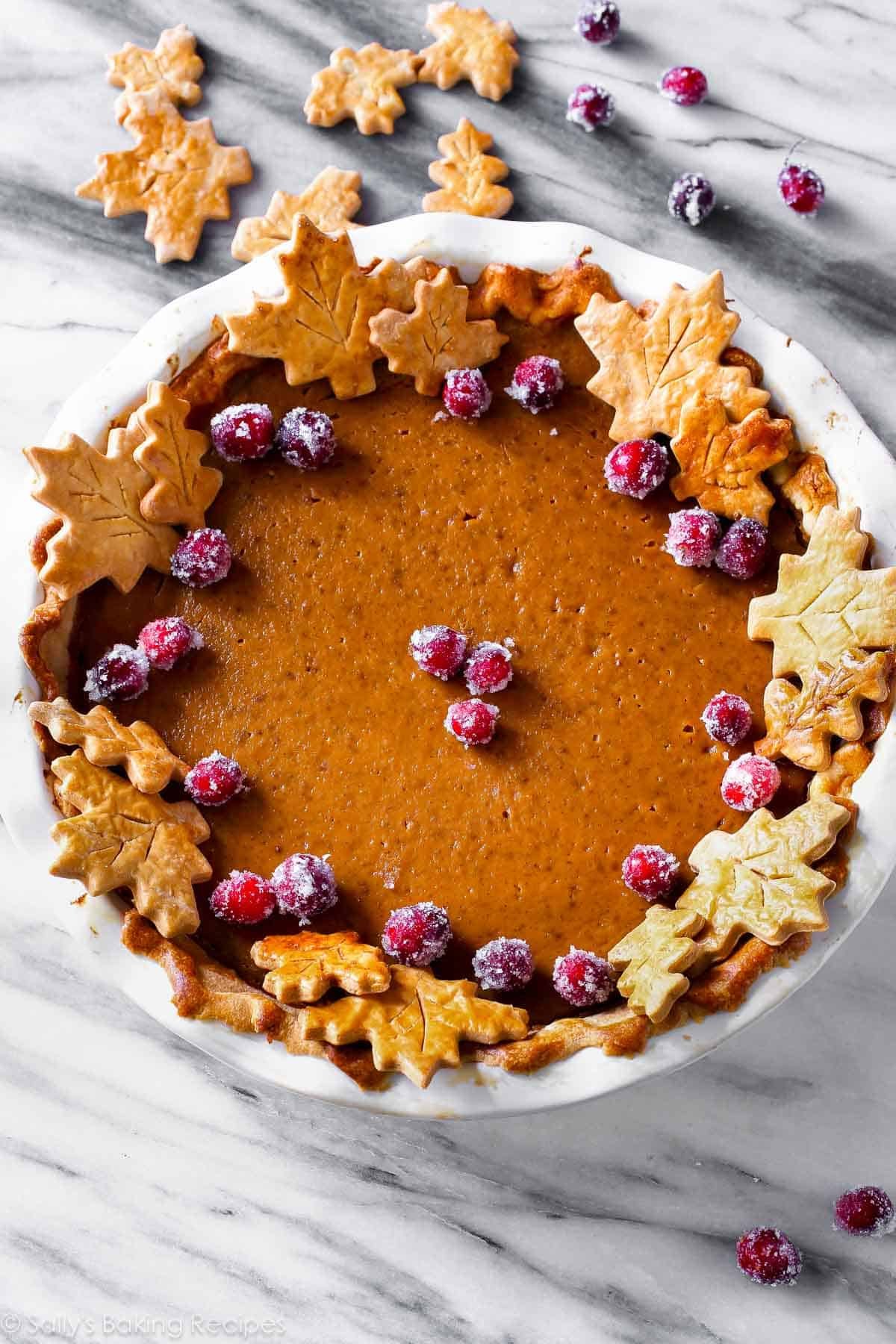 pumpkin pie with sugared cranberries and leaf pie crust cut outs.
