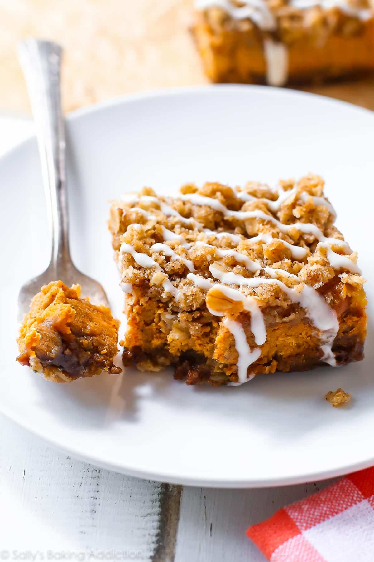 pumpkin streusel bar with vanilla icing on a white plate with a fork
