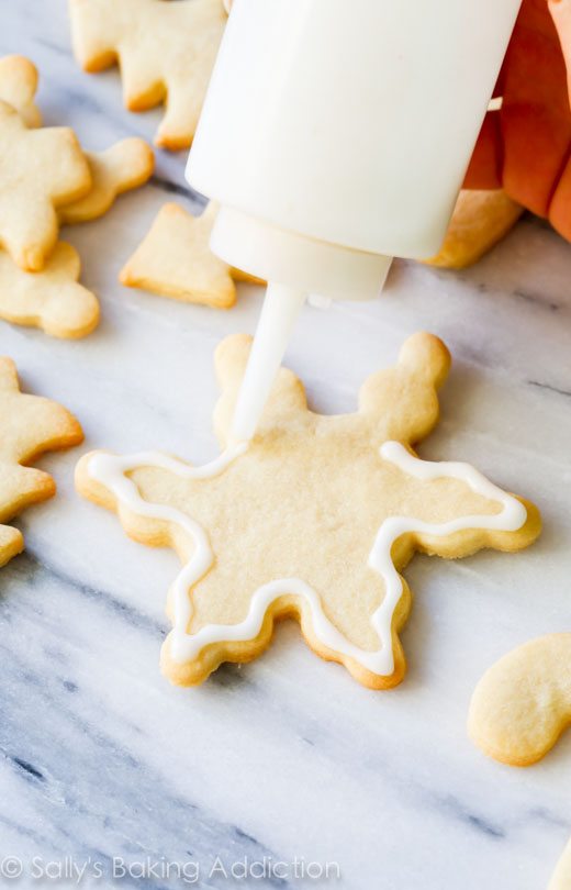 squeeze bottle piping white icing onto snowflake sugar cookies