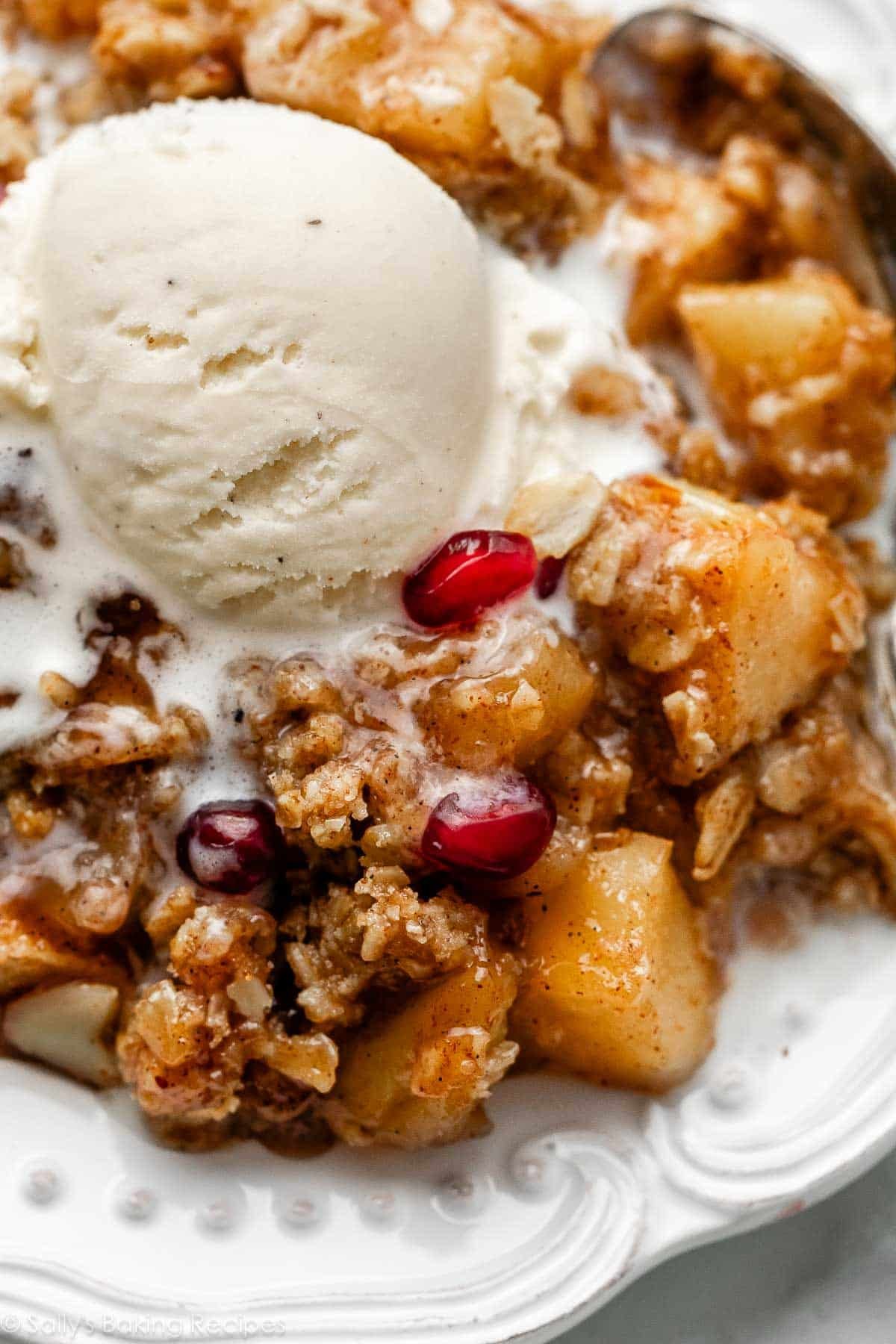 close-up serving of gluten free apple crisp and vanilla ice cream melting on top on white plate.