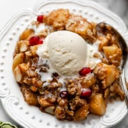 serving of gluten free almond apple crisp with ice cream on top on white plate.