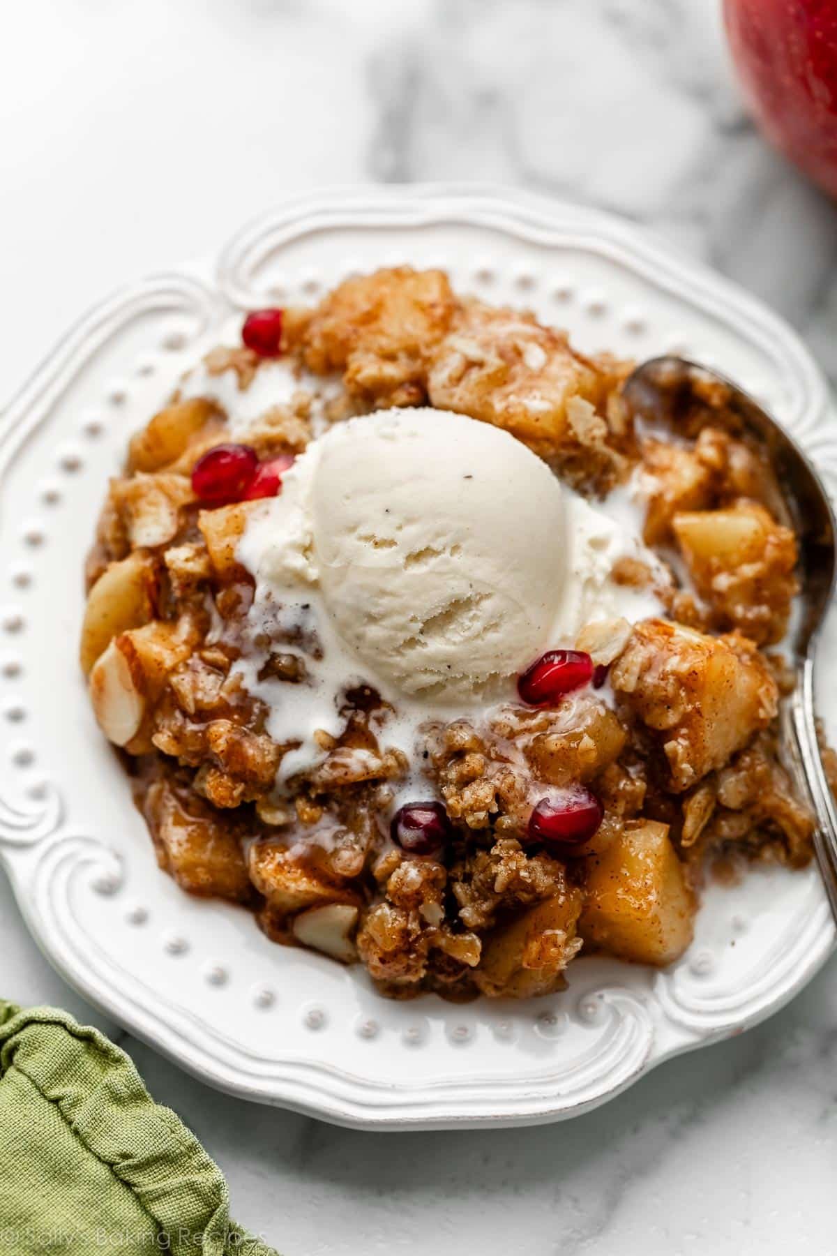 serving of gluten free almond apple crisp with ice cream on top on white plate.