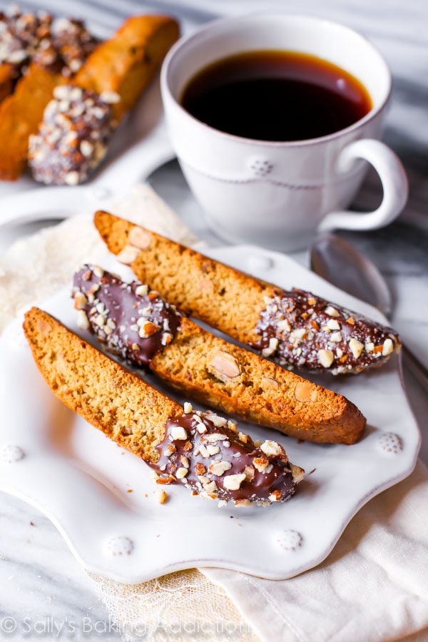 almond biscotti with part of each cookie dipped in chocolate on a white plate with a cup of coffee