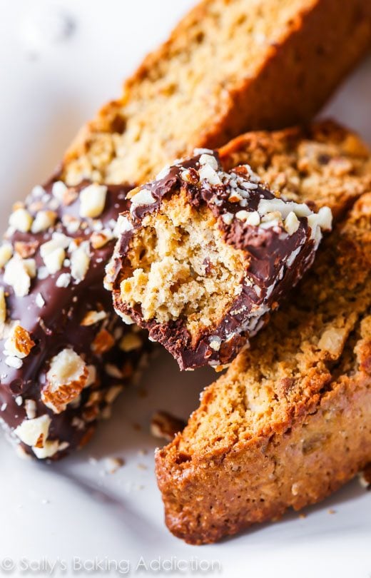 almond biscotti with part of each cookie dipped in chocolate with a bite taken from one biscotti showing the inside