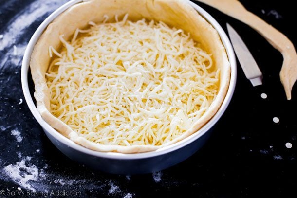 deep dish pizza dough in a pan with layer of cheese on the crust