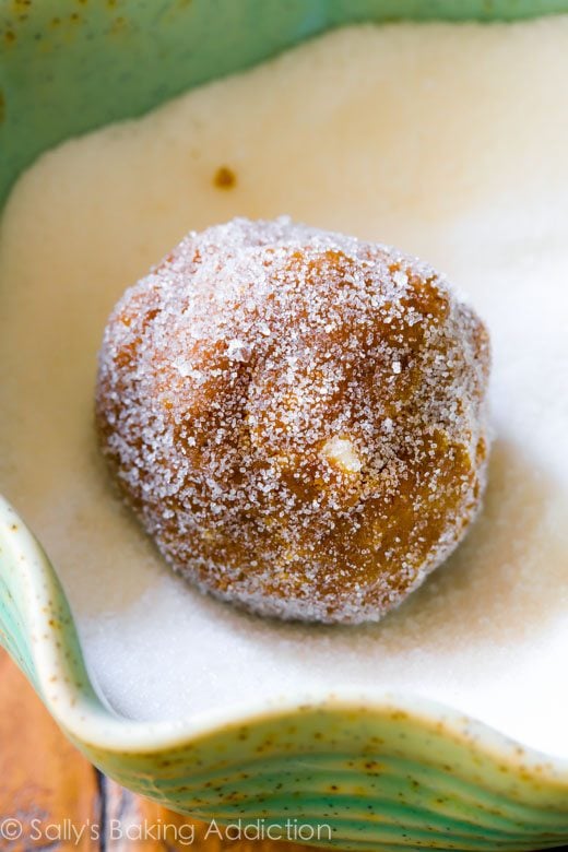 soft white chocolate chip molasses cookie dough ball rolled in a green bowl of granulated sugar