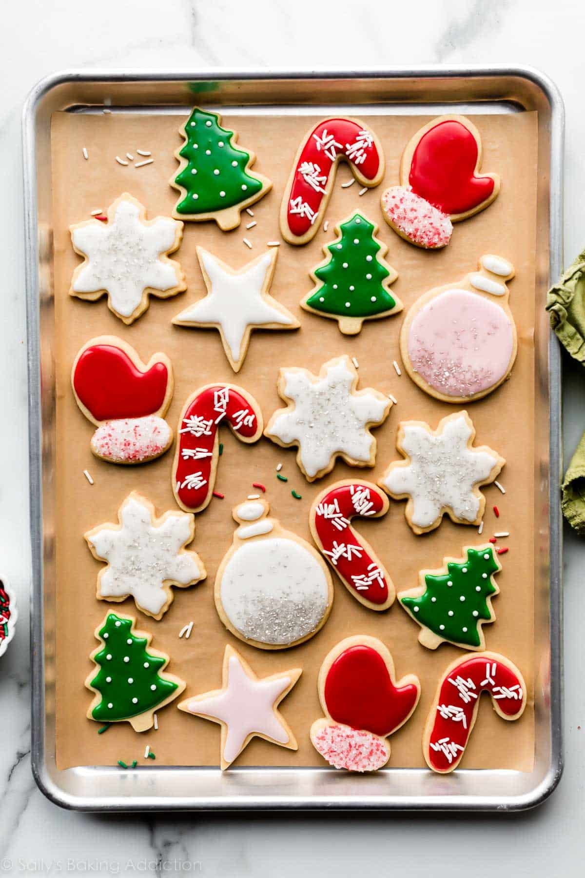 decorated Christmas sugar cookies including Christmas tree, red mittens and candy canes, ornaments, and snowflakes with icing.