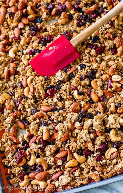 trail mix granola on a baking sheet with a red spatula