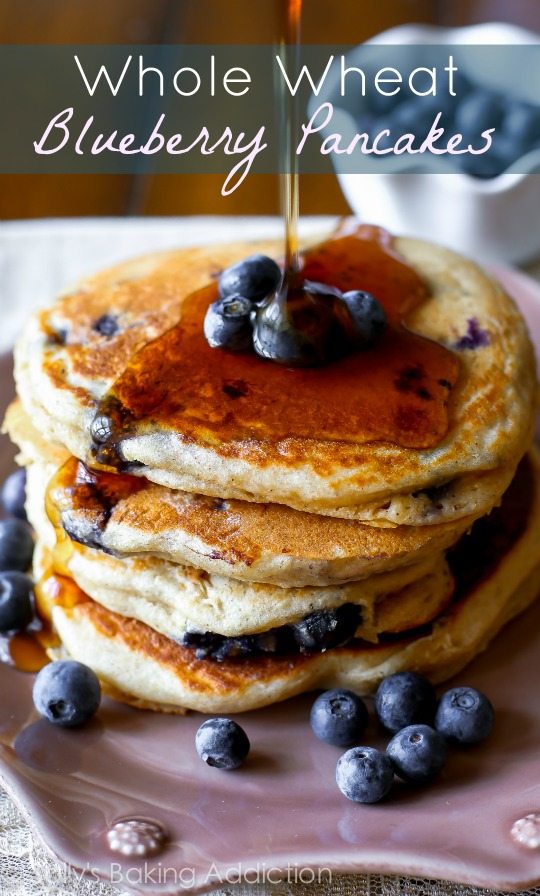 stack of whole wheat blueberry pancakes topped with maple syrup and fresh blueberries on a pink plate