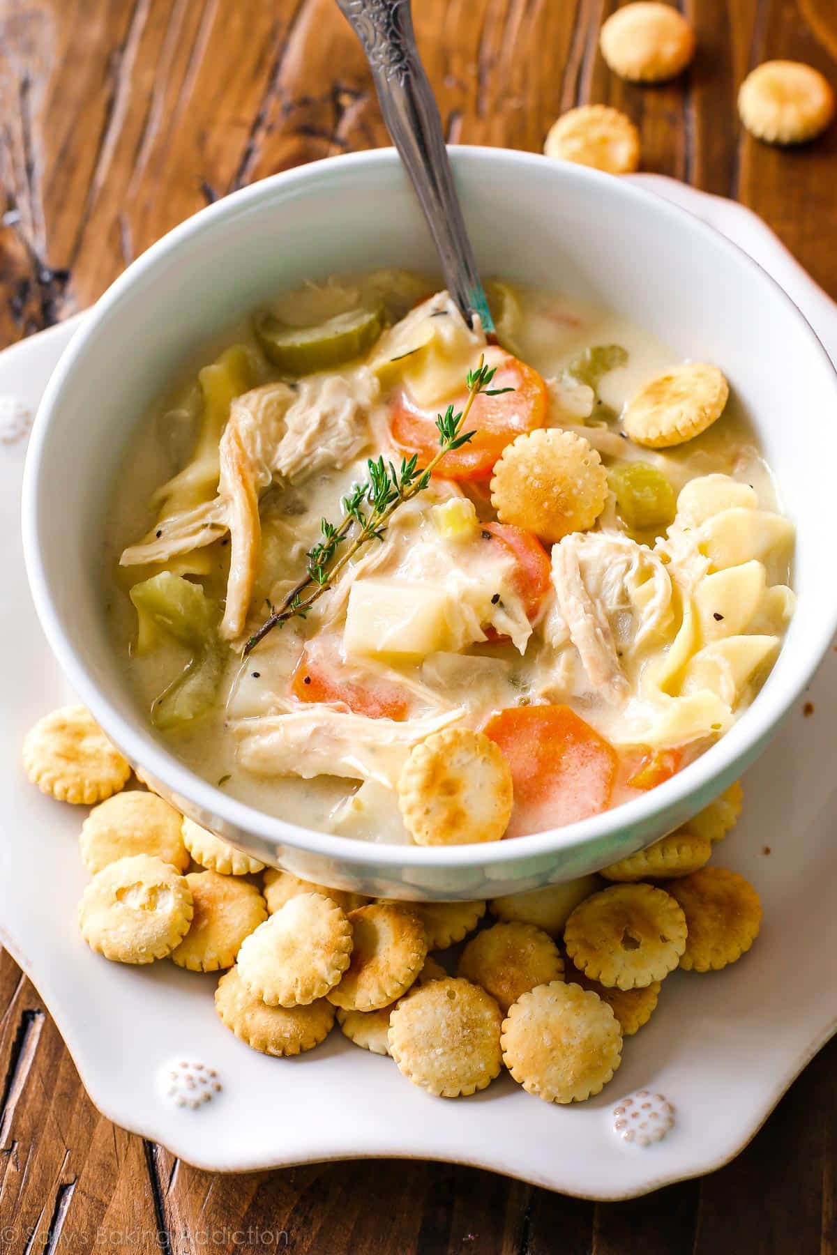 creamy chicken noodle soup in a white bowl on a white plate with oyster crackers