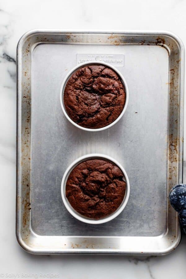 two baked chocolate cakes in ramekins on baking sheet.