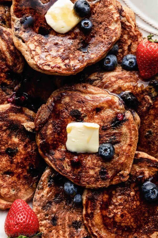 blueberry whole wheat pancakes with fresh blueberries, strawberries, maple syrup, and pats of butter.