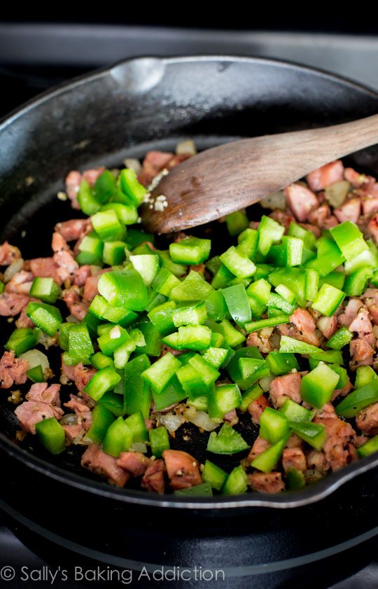 peppers and sausage sautéing in skillet with a wood spoon