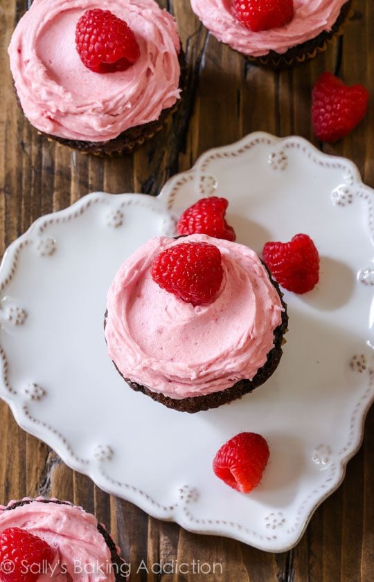 overhead image of chocolate cupcake topped with raspberry frosting and raspberries on a heart shaped white plate