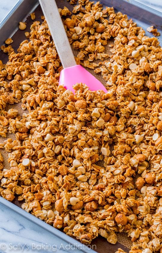 honey roasted peanut butter granola on a baking sheet with a pink spatula
