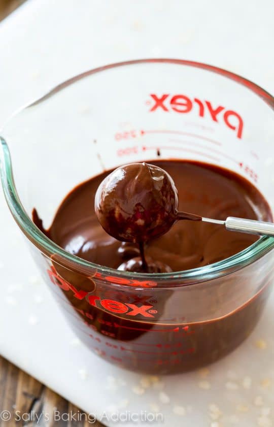 dipping a key lime truffle with a candy dipping tool into melted dark chocolate in a glass measuring cup