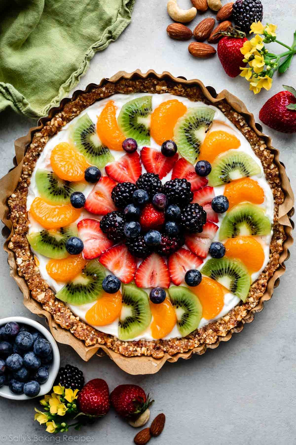 no bake fruit tart with yogurt inside tart pan on gray backdrop with strawberries and blueberries around it.