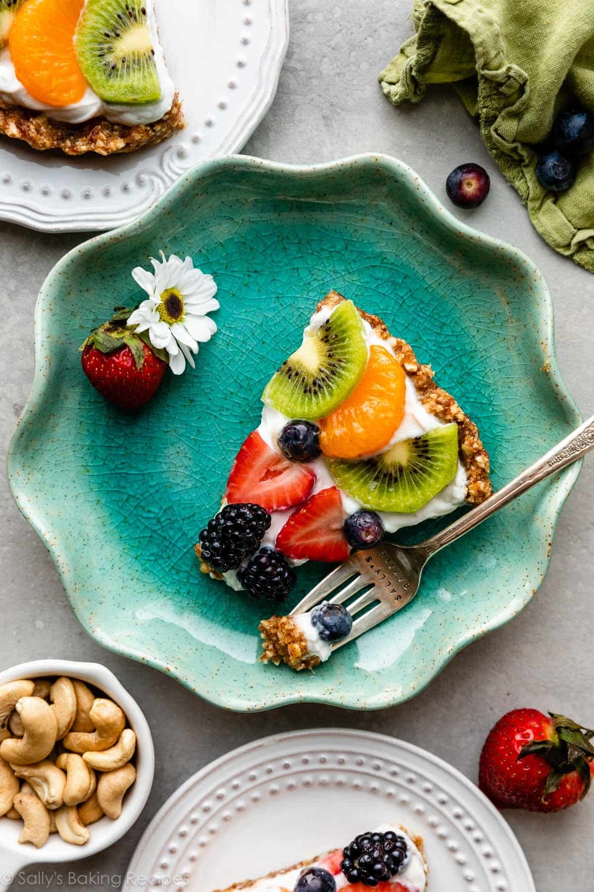 no bake Greek yogurt fruit tart slice with kiwi, mandarin orange, and berries on a blue plate with more slices on white plates around it.