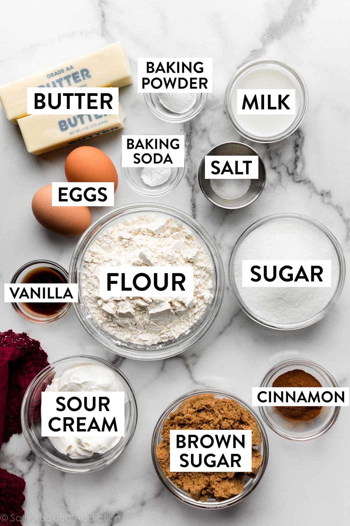 bowls in ingredients on marble counter including flour, sugar, milk, brown sugar, cinnamon, and more.