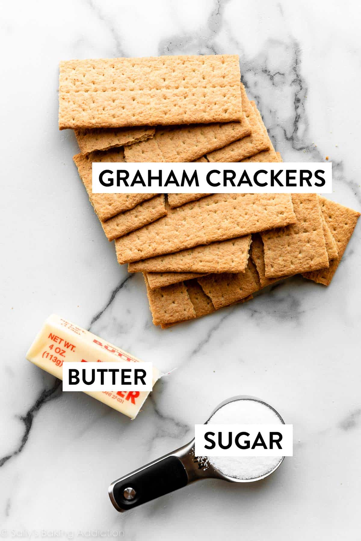 graham crackers, butter, and sugar in measuring cup on marble countertop.