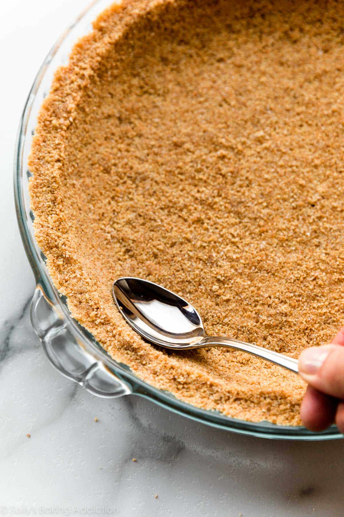 hand using a spoon to smooth and round out graham cracker crust mixture.