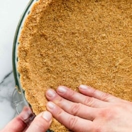 two hands pressing graham cracker crust into glass pie dish.