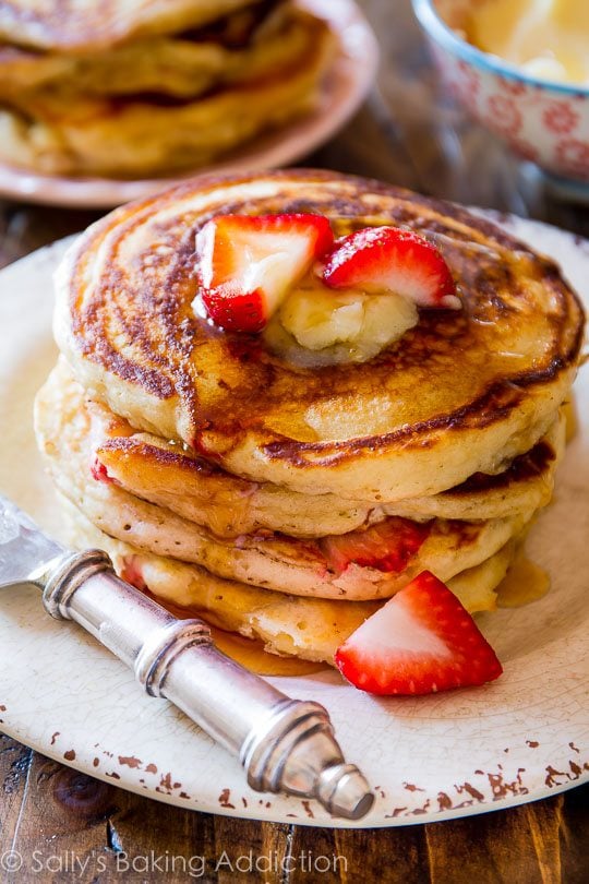 stack of strawberry buttermilk pancakes topped with honey butter and sliced strawberries on a white plate