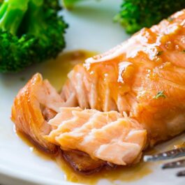 garlic honey ginger glazed salmon on a white plate with a fork and broccoli