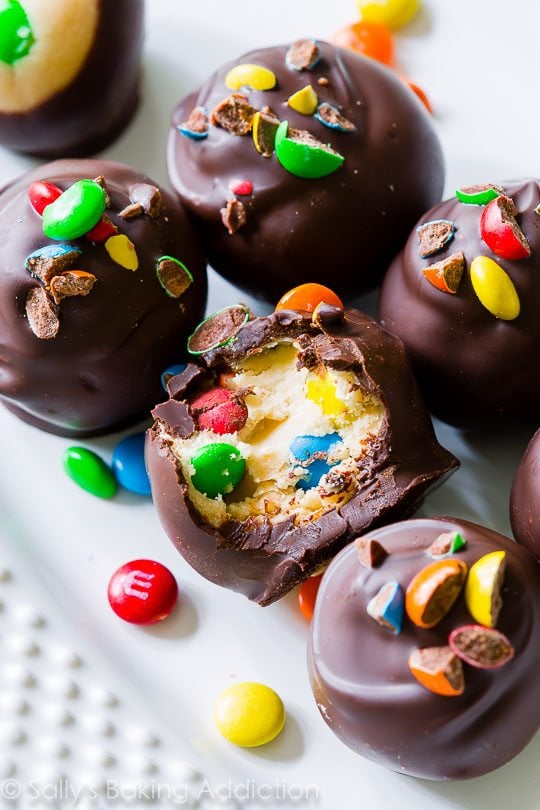Peanut Butter M&M Truffles on a white serving tray with a bite taken out of one truffle showing the inside