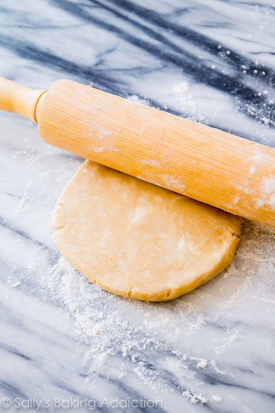 disc of pie dough with a wood rolling pin