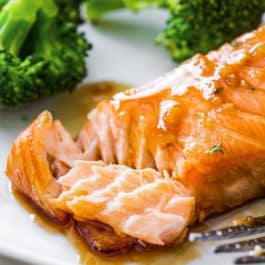 honey garlic glazed salmon on white plate with broccoli in background.