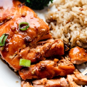 close-up of honey garlic soy glazed salmon with green onion, brown rice, and broccoli on plate.
