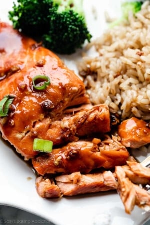 close-up of honey garlic soy glazed salmon with green onion, brown rice, and broccoli on plate.